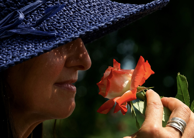 Eine Frau mit Hut riecht eine Rose